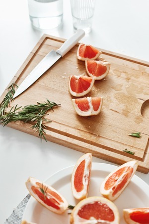 Close up of grapefruit pieces knife and rosemary on wooden desk. Copy space.の写真素材