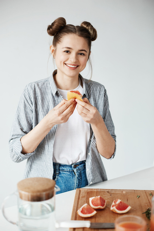 Beautiful girl smiling looking at camera holding grapefruit peace over white wall. Healthy fitness nutrition.の写真素材