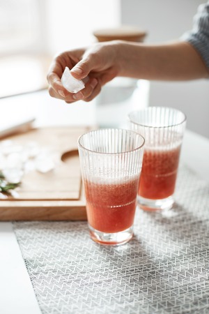 Close up of girls hands putting ice pieces in glasses with grapefruit detox healthy smoothie.の写真素材