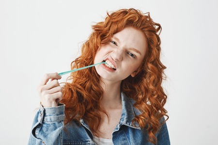 Young cool brutal redhead girl in jean jacket chewing gum looking at camera over white background.の写真素材