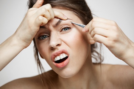 Young pretty girl with perfect clean skin 
tweeze eyebrows making funny face over white background. Beauty and spa.の写真素材