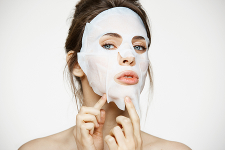 Young girl with facial mask looking at camera over white background. Cosmetic procedure. Beauty spa and cosmetology.の写真素材