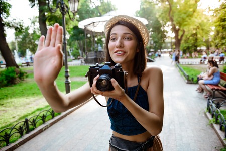 Beautiful brunette girl in hat smiling, taking pictures in park.の写真素材