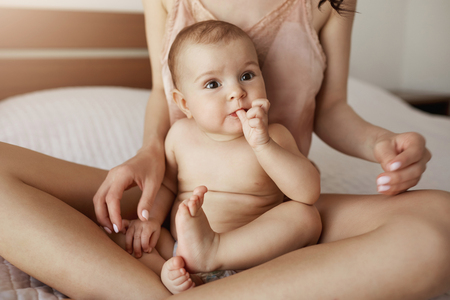 Close up of young mother in sleepwear and her newborn baby sitting on bed in morning smiling playing together.の写真素材