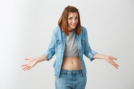 Portrait of young pretty brunette girl looking at camera shrugging over white background.の写真素材