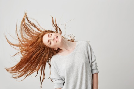 Portrait of young cheerful beautiful redhead girl smiling with closed eyes shaking head and hair...
