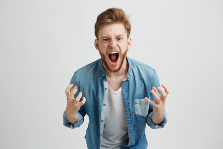 Angry rage young man with beard shouting screaming gesturing over white background.の写真素材