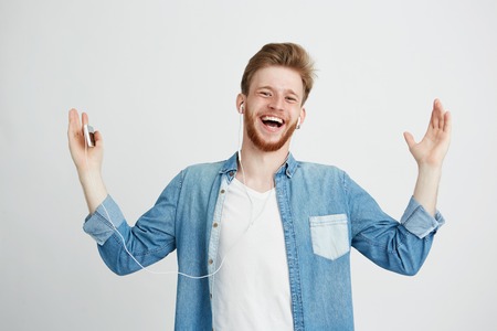 Happy young man smiling listening to streaming music in headphones singing looking at camera over white background.の写真素材