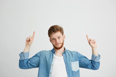 Portrait of young handsome man looking at camera pointing finger up over white background.
