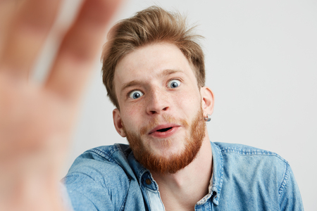 Surprised young man with beard in jean shirt stretching hand to camera over white background.の写真素材
