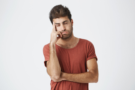 Tired spanish bearded man wearing red t-shirt holding hand on forehead looking stressful having headache after conflict situation on work. People, stress and migraine.の写真素材