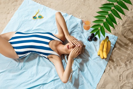 Tanned young woman taking unhealthy sunbath on a summer day on a beach hiding from the sun with...