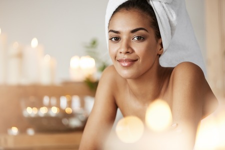 Portrait of beautiful african girl with towel on head smiling resting in spa salon.の写真素材