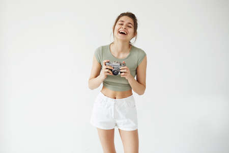 Portrait of cheerful happy young female photograph laughing holding old camera over white wall.の写真素材