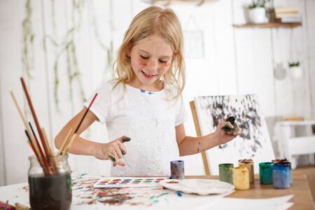 Laughing girl full of joy with hands in paint in art room. Cheerful child drawing picture with smile. Delighted kid radiates positive emotions and happiness.の写真素材