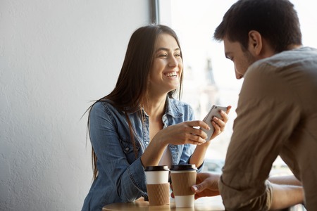 Cheerful beautiful girl with dark hair sits in cafe on date, laughing and telling funny stories from life to her boyfriend. Warm atmosphere of happinessの写真素材