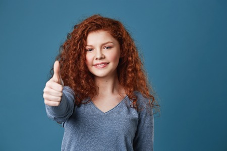Attractive redhead girl with freckles showing thumb up in camera with happy and delightful expression. Copy spaceの写真素材