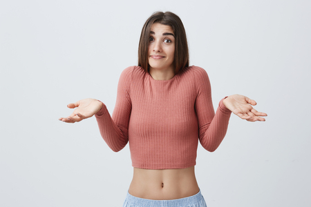 I have no idea. Portrait of young attractive sexy caucasian student girl with dark long hair in pink shirt and blue sport shorts spreading hands with confused and unsure expression when friend asks her about exam results.の写真素材