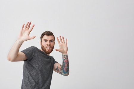 Portrait of young good-looking unhappy tattooed european hipster man with beard and stylish short...