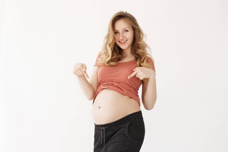 Portrait od joyful happy mama with blond hair in red t-shirt smiling brightfully, pointing on her...