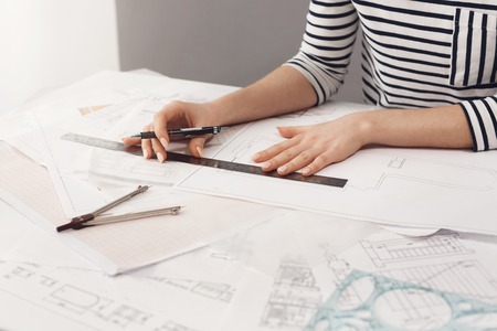 Close up detail of beautiful young female architect in striped shirt sitting at desk, holding pen...