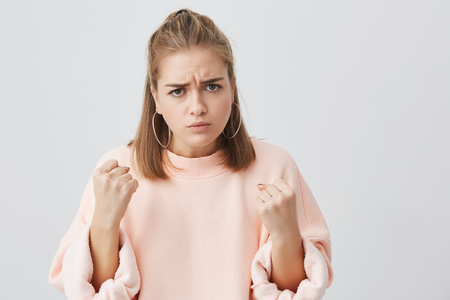 Close up portrait of angry dissatisfied european young female frowning her face, holding fists in front of her, ready to fight or defend herself. Aggresive, emotional female, feeling insulted.の写真素材
