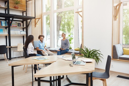 Group of three young multi ethnic startups working together in coworking space, having break from...