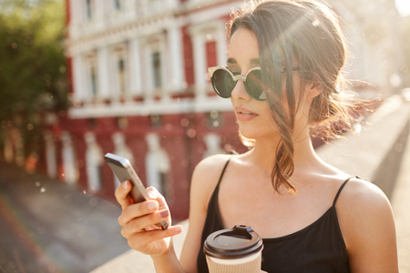 Close up portrait of young good-looking serious hispanic woman chatting with friend that being late for meeting on cell phone, drinking coffee, spending sunny summer day outside.の写真素材