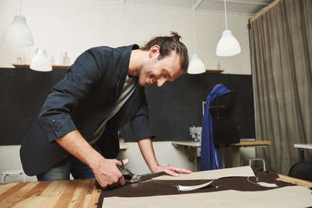 Mature joyful attractive dark-haired hispanic, male fashion designer working on new dress in...