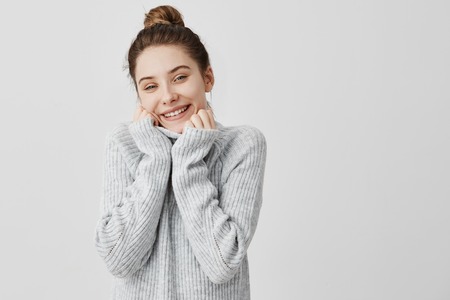 Headshot of adorable smiling woman wrapping up her face in collar of grey sweater. Female artist expressing appeasement and comfort. Feelings conceptの写真素材