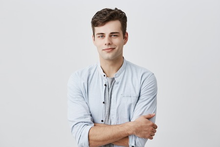 Handsome attractive young european man in casual shirt with dark hair and blue eyes, keeping arms foldedの写真素材
