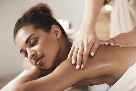 Attractive african girl having massage relaxing in spa salon. Closed eyes.の写真素材