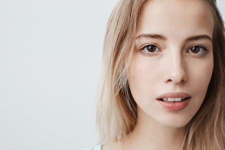 Close up portrait of pretty good-looking european female with pure healthy skin, looks pensively at camera with slightly parted lips, thinks or remembers pleasant moments of life.の写真素材