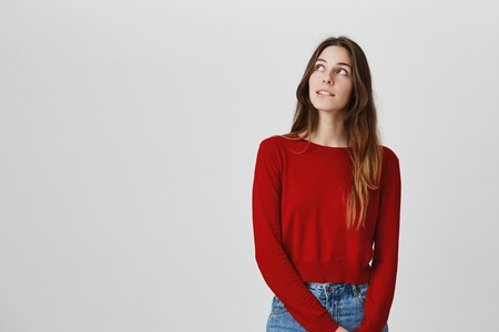 Close up portrait f young european girl with long brown hair in red jumper and jeans looking aside, biting lip, dreaming about date with guy from university.の写真素材