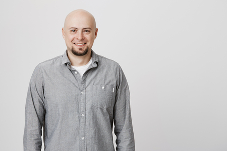 Portrait of bald adult man with beard standing casually over white background wearing gray shirt. Attractive male talking to his friend smiling cheerfully enjoying with their conversation.の写真素材