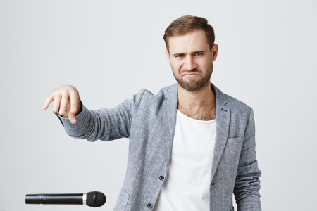 Stylish hipster guy with beard wears trendy clothes, prepares for music concert, rehearses, uses microphone and throws it away in despair and frustration. Negative emotions and face expression.の写真素材