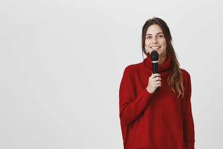 Microphone, music, songs, leisure time concept. Good-looking caucasian female singer looks at camera happily, holds microphone in her hand, smiles broadly. Positive smiling woman singingの写真素材