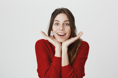 Portrait of pensive dark-haired dreamy hipster with ponytail imagines something in her mind, looks happily at camera, smiles, rests her head on hands. Attractive young female dreams about weekendsの写真素材