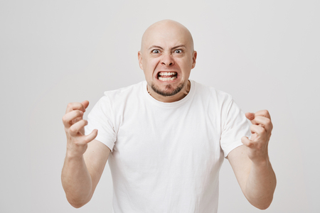 Angry and insane bald bearded guy expressing his readiness to kill somebody, being filled with anger and negative emotions, standing over gray background and gesturing. Employer is madの写真素材