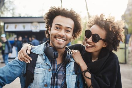 Positive and emotive young african-american people cuddling or hugging while walking in park, joking and being in good mood, wearing trendy outfit. Friendship lasts foreverの写真素材