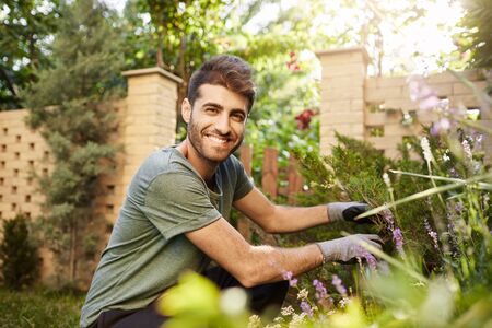 Close up portrait of attractive mature bearded hispanic florist smiling in camera, watching over flowers in garden near countryside house with happy and relaxed face expressionの写真素材