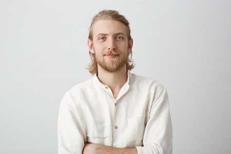 Portrait of positive handsome blond man with beard and moustache, standing with crossed hands in white shirt with slight smile and confident expression. Boyfriend picking flowers for his coupleの写真素材