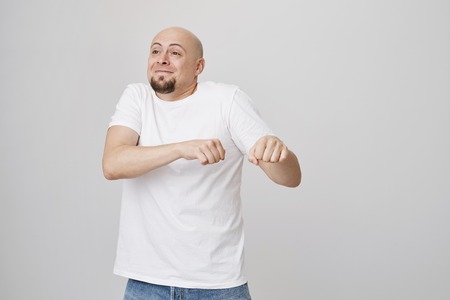 Indoor portrait of funny excited bald caucasian guy making dance move as if celebrating something, being in great mood while standing over gray background. Man is happy he will go on vacationの写真素材