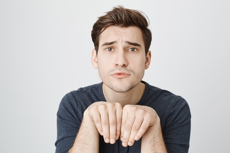 Shot of funny positive man with dark hair in casual clothes holding hands like a puppy, having...