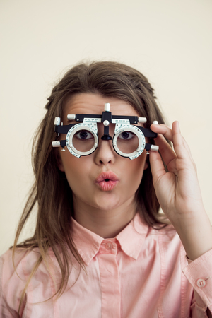 Horizontal shot of excited cute european brunette checking vision with phoropter, being interested in how it works, waiting for optometrist to prescribe appropriate glassesの写真素材