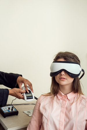 Horizontal portrait of cute european female patient sitting in eye specialist office, wearing digital vision screener while testing sight, waiting for optometrist to finish check-upの写真素材