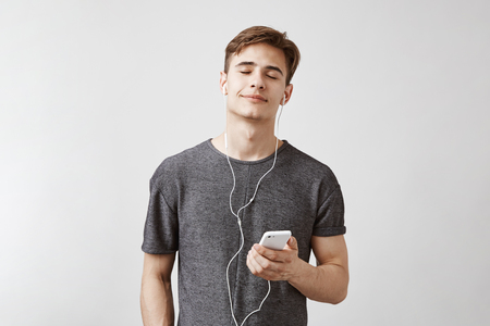 Young good looking male enjoying listening to the new track. Man looks relaxed and pleased hearing song that makes him remember all beautiful moments of this day.の写真素材