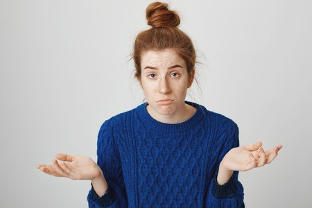 There is nothing I can do. Indoor shot of gloomy confused woman with red hair and freckles in winter sweater shrugging with spread palms, having no idea how to solve problem, having no interestの写真素材