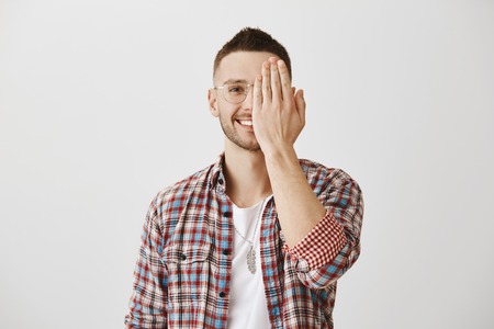 People emotions concept. Portrait of attractive man in glasses hiding half of face with palm while...