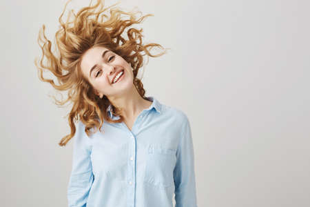 Happy good-looking female office worker with curly hair waving head and smiling at camera,...